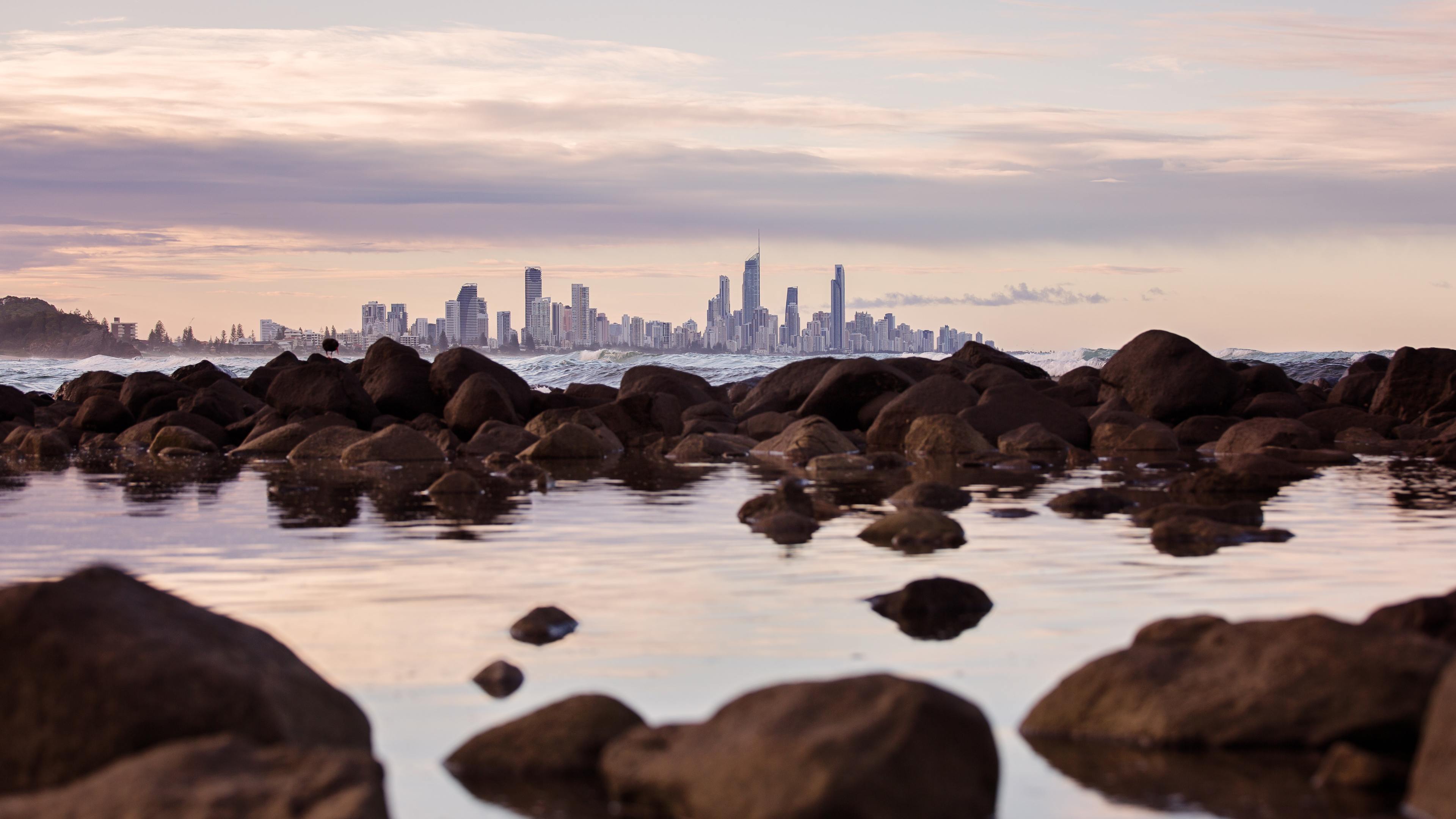 seashore rocks near city view of buildings 5k 1540143476