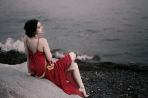 girl in red dress sitting on rocks beach 1575665092